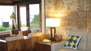 A cozy living room with a sofa, a coffee table, and a lamp. There is a window with a view of greenery outside.