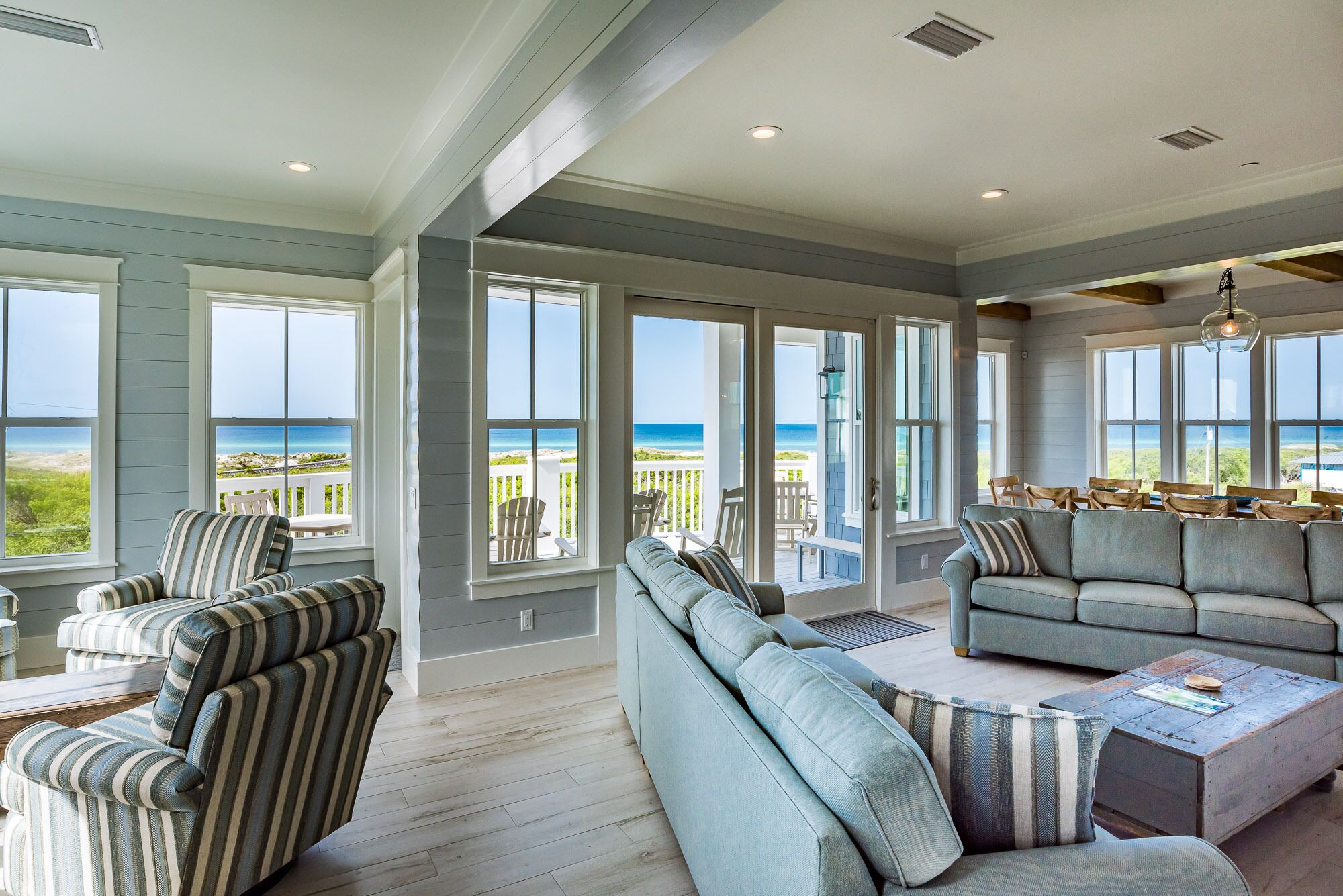 A spacious living room with large windows offering ocean views, a cozy seating area, and a wooden coffee table.