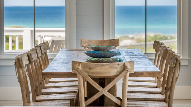 A wooden dining table with a view of the ocean through large windows.