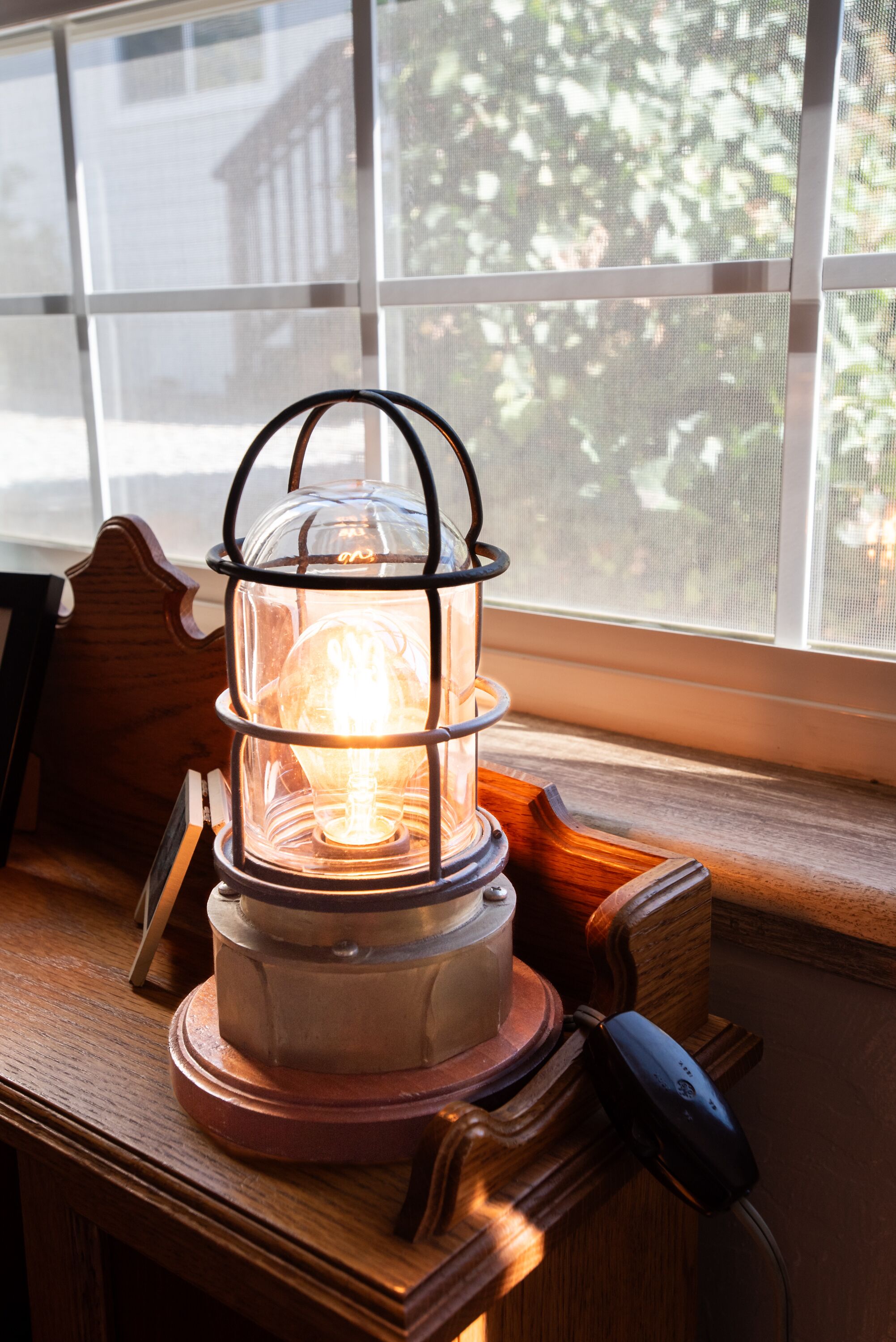 A table with a lit lantern, a wooden bench, and a window with a view of trees.