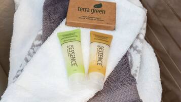 A bathroom with a white towel, a gray towel, and two bottles of Terra Green body bar and conditioner.