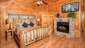 Een slaapkamer in een blokhut met een bed, een open haard, een televisie en houten wanden.