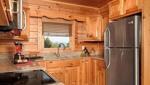 Een keuken met houten kastjes, een roestvrijstalen koelkast, granieten aanrechtbladen en een raam met jaloezieën.