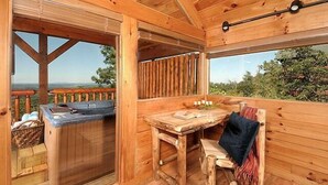 Een houten vakantiehuis met een jacuzzi, een tafel en een bank.