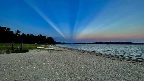 Een strand met een kano, kalm water en een heldere lucht.