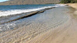 Une plage à l’eau claire, un promontoire rocheux et une montagne en arrière-plan.