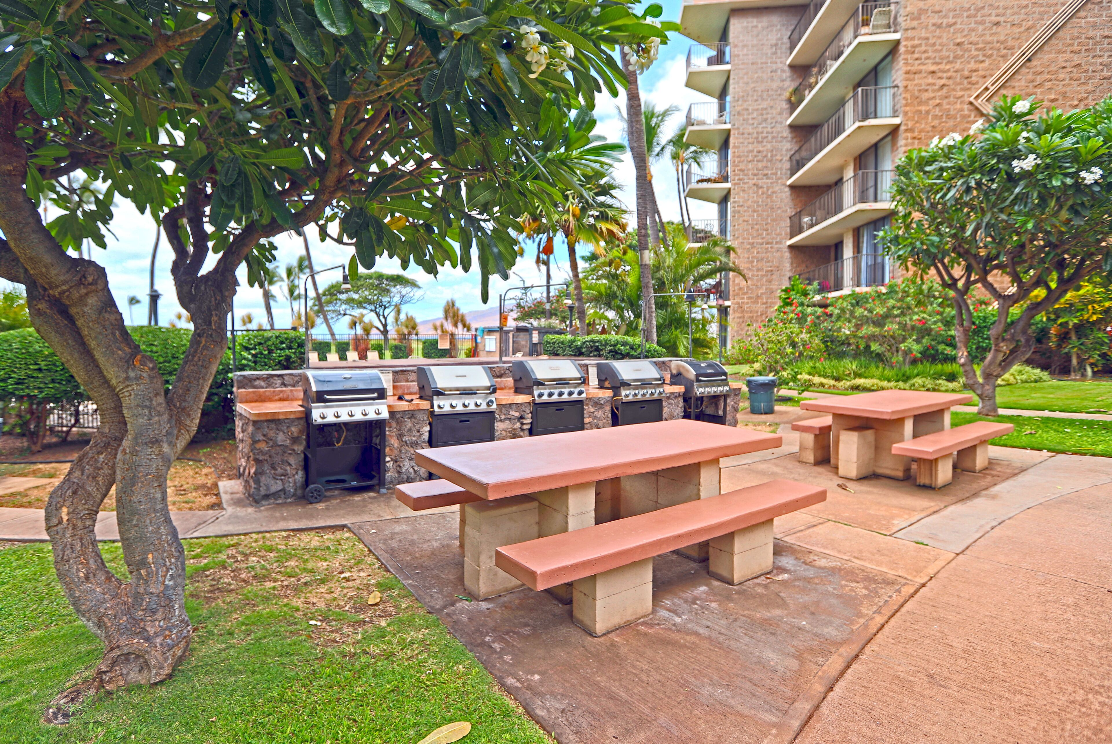 An outdoor patio with a barbecue grill, picnic tables, and a building in the background.