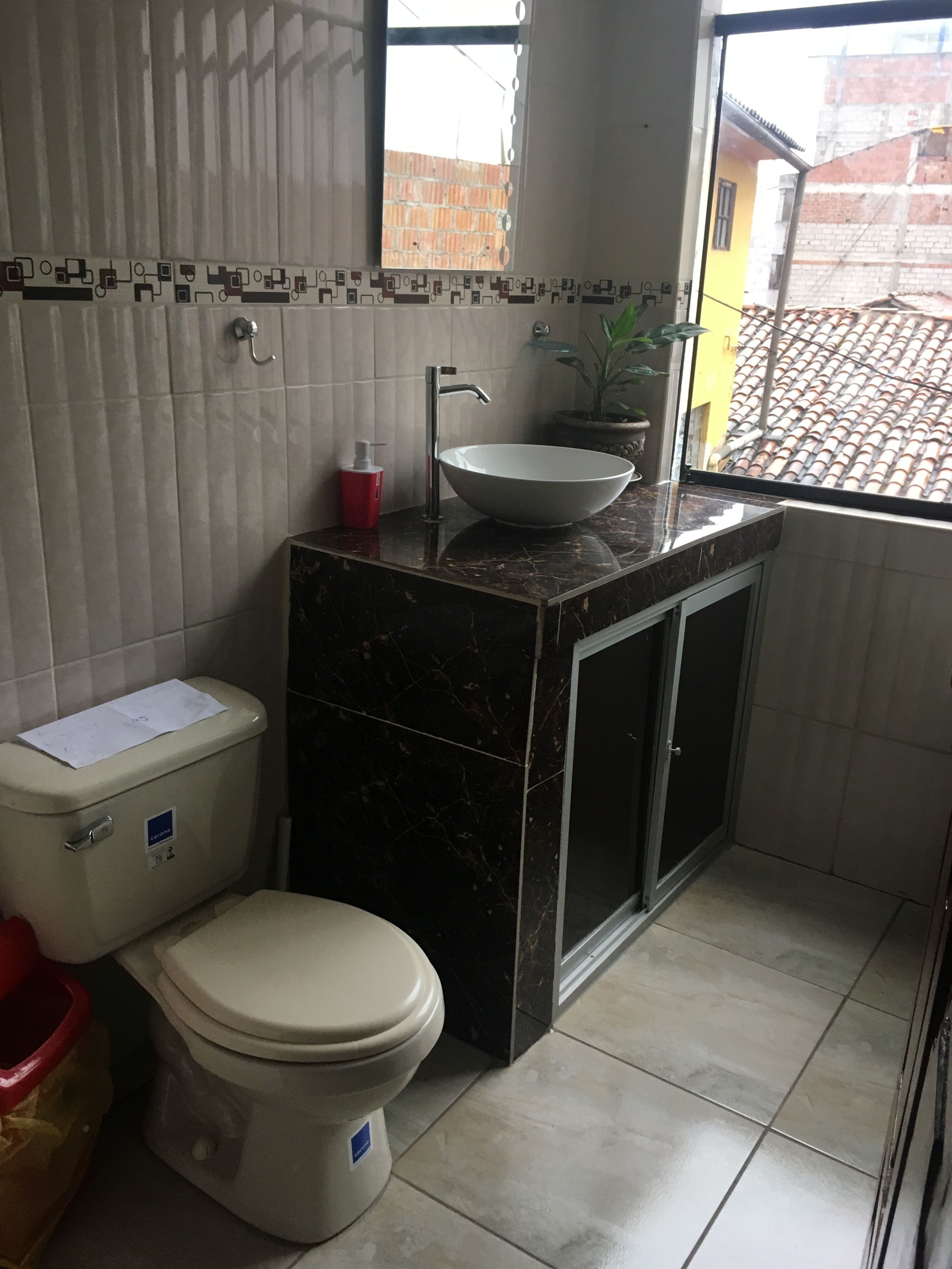 Un baño pequeño con inodoro, lavabo y ventana con vistas a una obra en construcción.