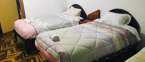 Two single beds with headboards, a wooden floor with a geometric pattern, and a plain white wall.