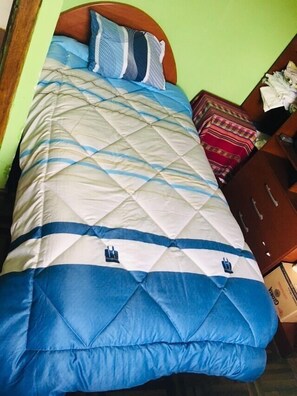Una cama con un estampado azul y blanco acolchado, cabecera de madera y pared verde.