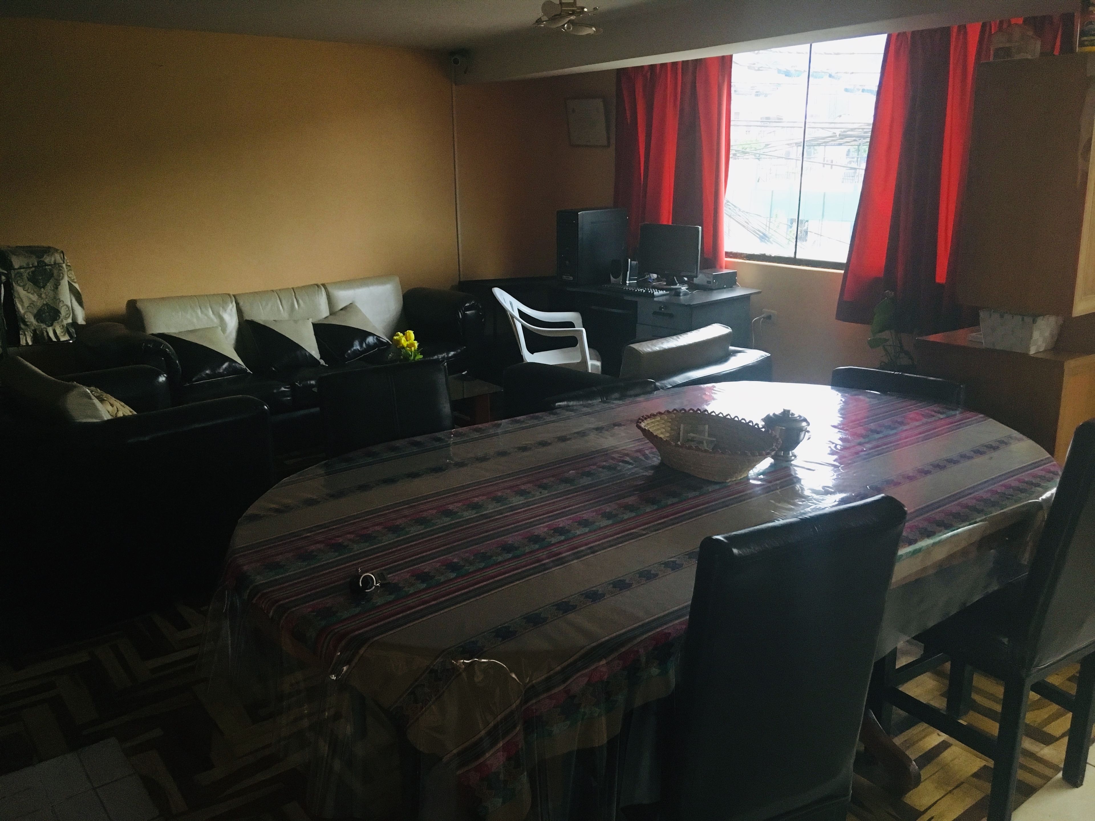 A living room with a sofa, a dining table with a patterned tablecloth, and a television in the background.