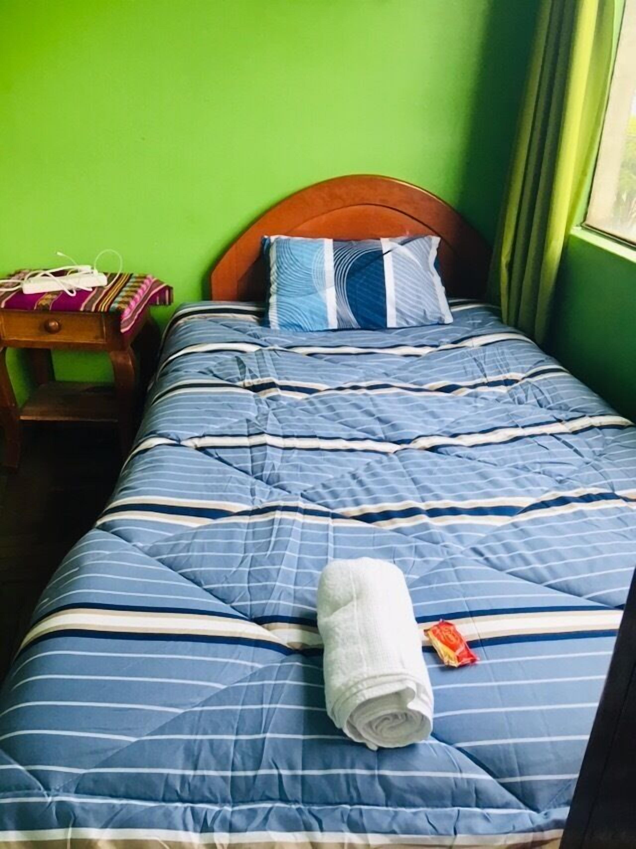A single bed with a blue striped bedspread, a wooden headboard, and a pillow with blue and white stripes. A rolled towel and a red object are on the bed.