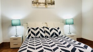 A neatly made bed with a geometric patterned bedspread, two bedside tables with lamps, and a cityscape painting on the wall. - Boston Luxury Suits Cottage for up to 24 guests!!! (Boston)