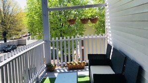 A covered patio area with a white railing, green artificial turf, a white table, and black wicker furniture. - Boston Luxury Suits Cottage for up to 24 guests!!! (Boston)