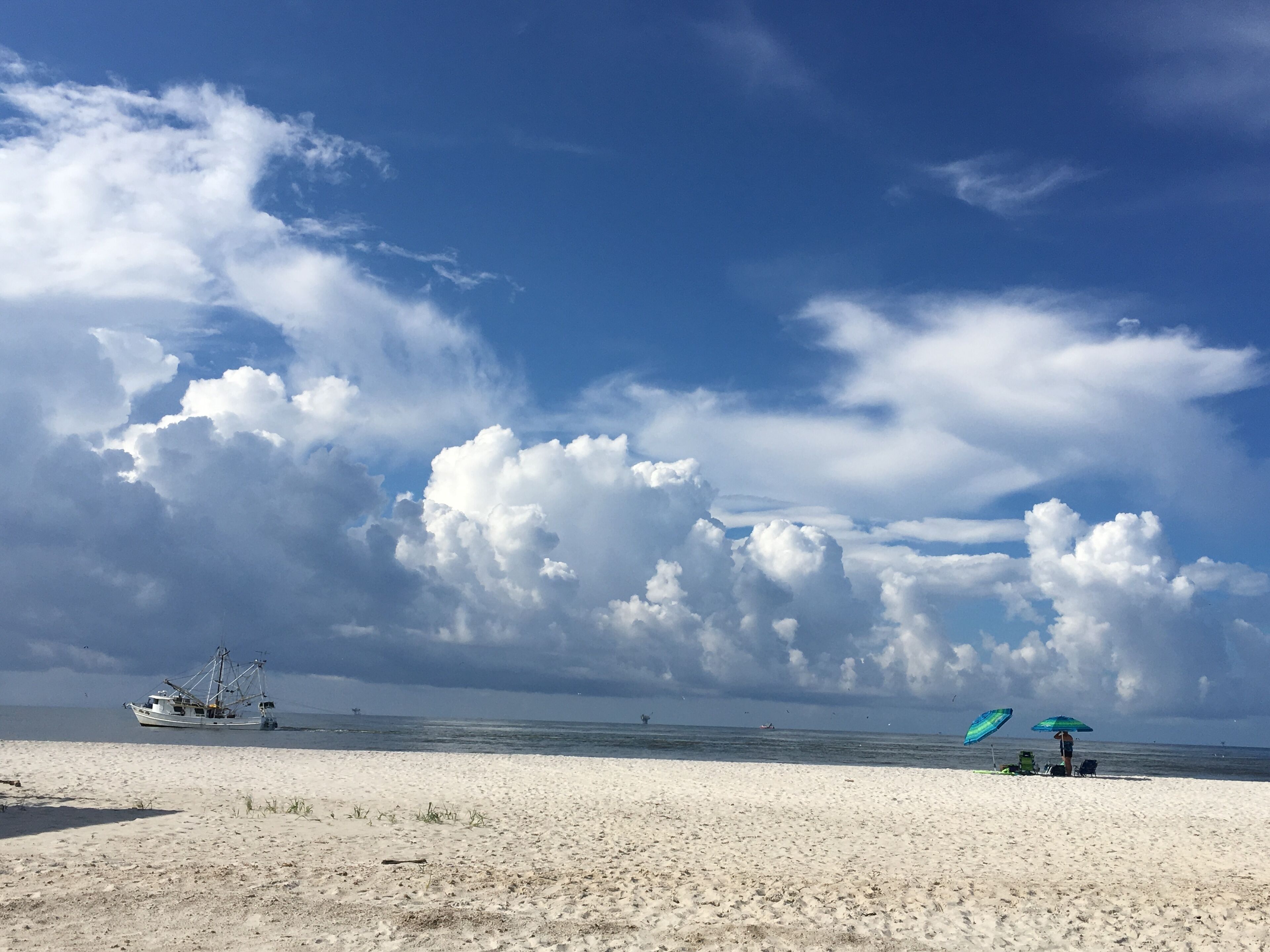 A beach with a fishing boat, a person with an umbrella, and a clear sky.