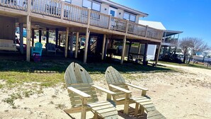 Eine hölzerne Deckterrasse direkt am Strand, mit überdachter Sitzecke und einem Gebäude im Hintergrund.