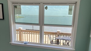 Ein Zimmer mit großem Fenster mit Blick auf einen Strand, einer Holzdielen-Terrasse und einem Elektrowerkzeug auf dem Boden.
