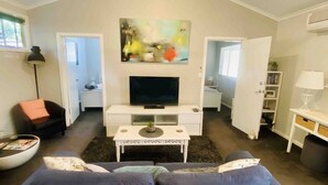 A living room with a flat-screen TV on a white console, a sofa, a coffee table, and a painting on the wall. - ADEL HILLS ESCAPE Clean•Cosy•Relax•Free Netflix (Woodside)