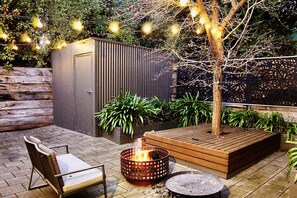A patio with a fire pit, a wooden bench, and a chair. There is a shed in the background and string lights above. - ADEL HILLS ESCAPE Clean•Cosy•Relax•Free Netflix (Woodside)