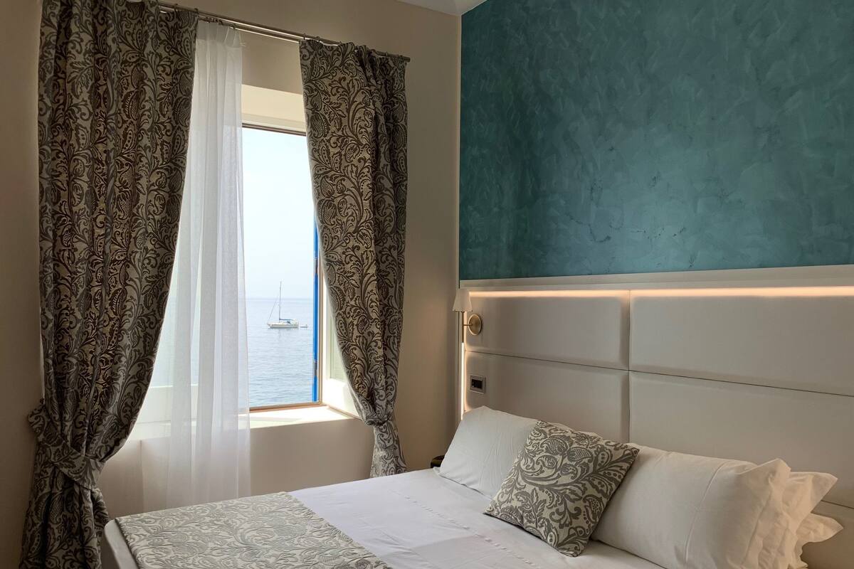 Ein Hotelzimmer mit Bett, Meerblick und einer wandfarben türkisen Wand.