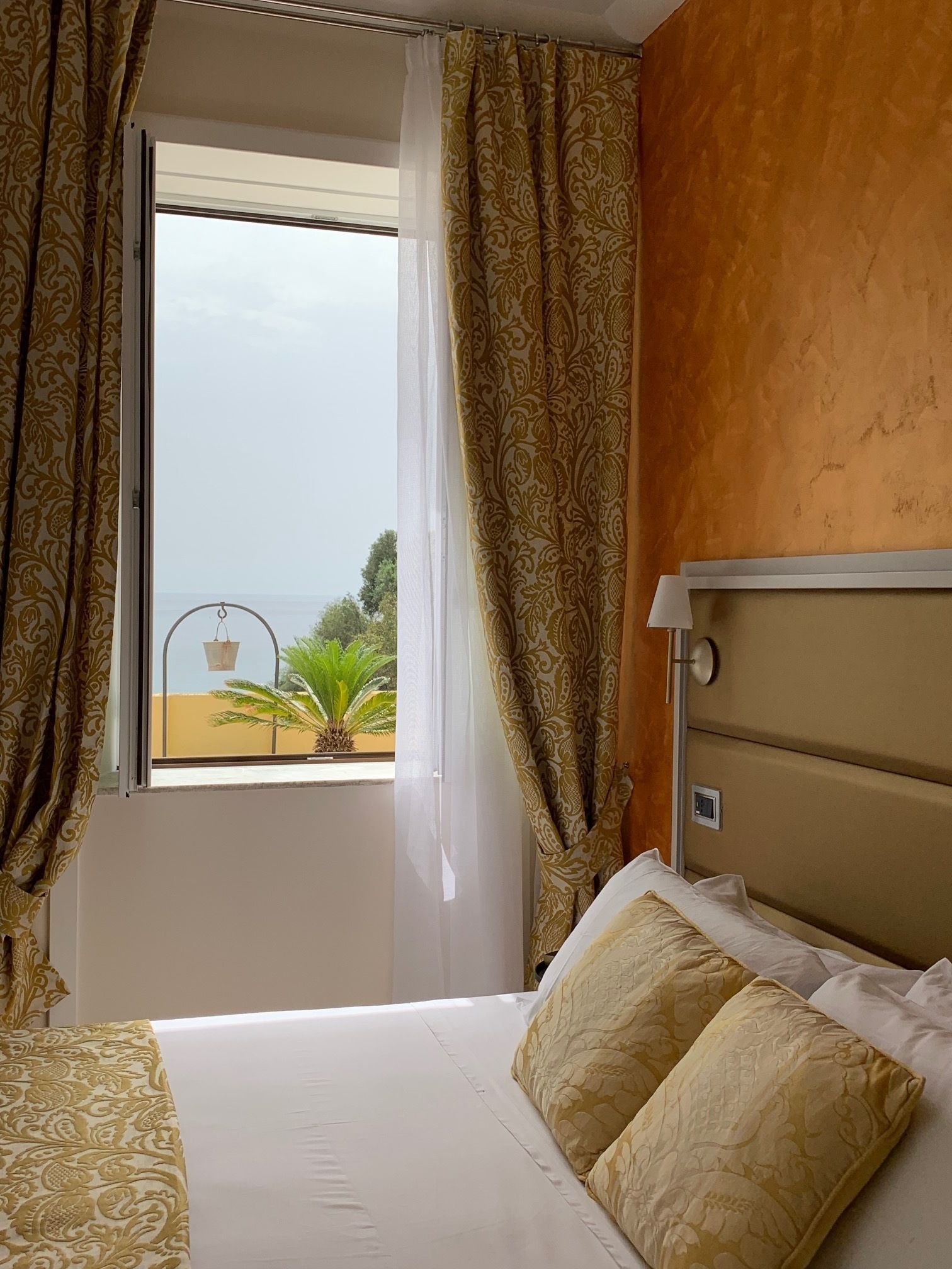 Una camera d'albergo con un letto, una finestra con tende e vista sul verde.