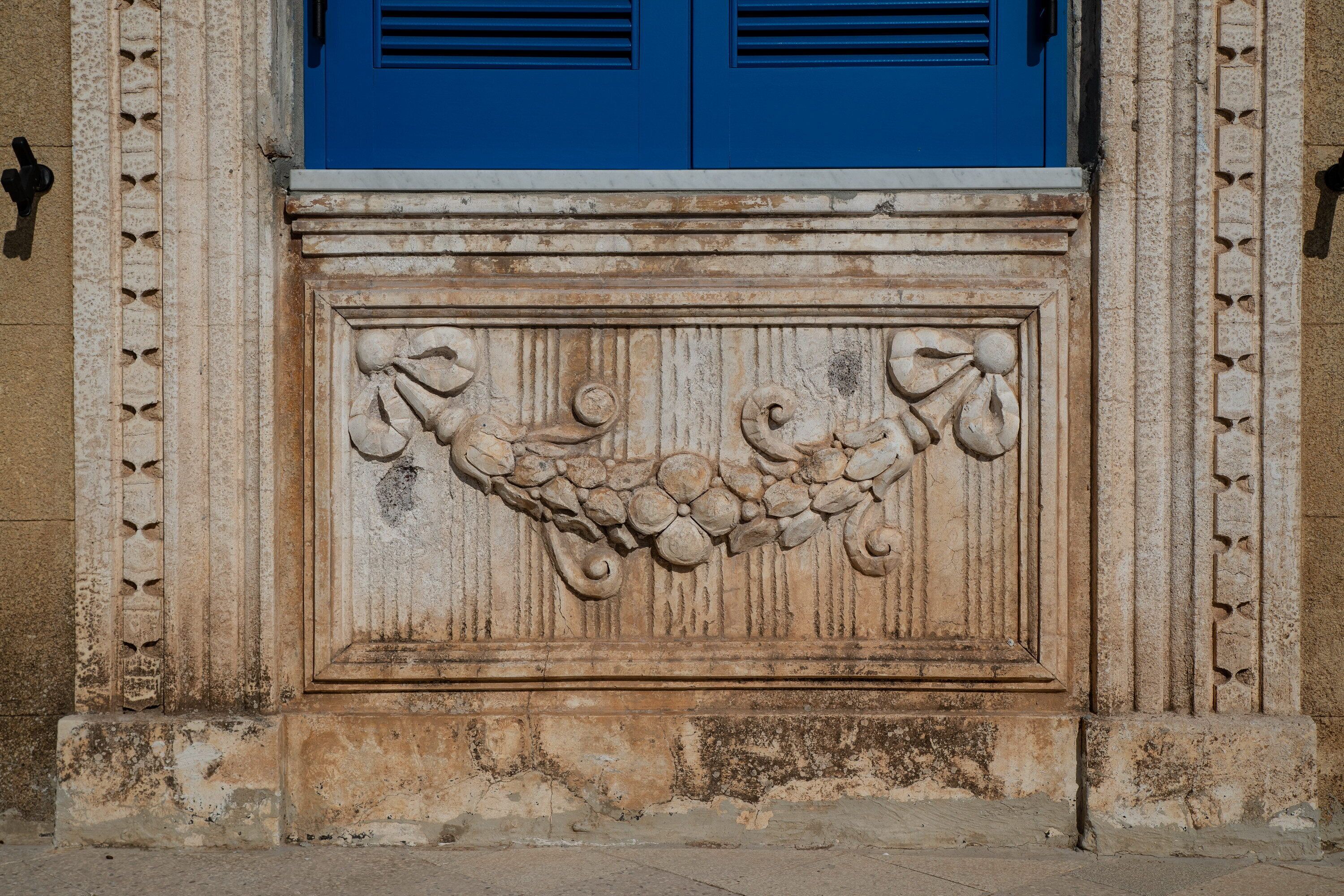 A stone relief with a grapevine design, flanked by two blue doors with shutters.