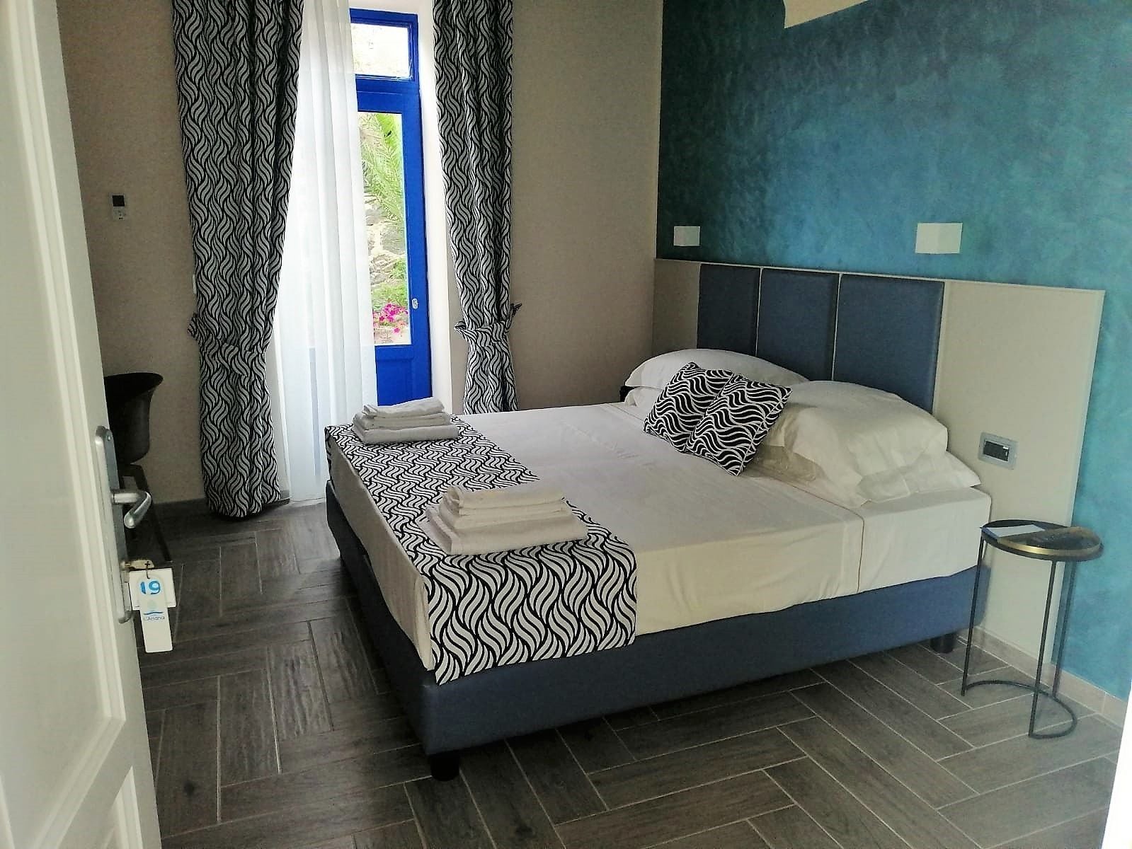 Une chambre à coucher avec un lit, des rideaux, une table de chevet et une vue sur l’extérieur.