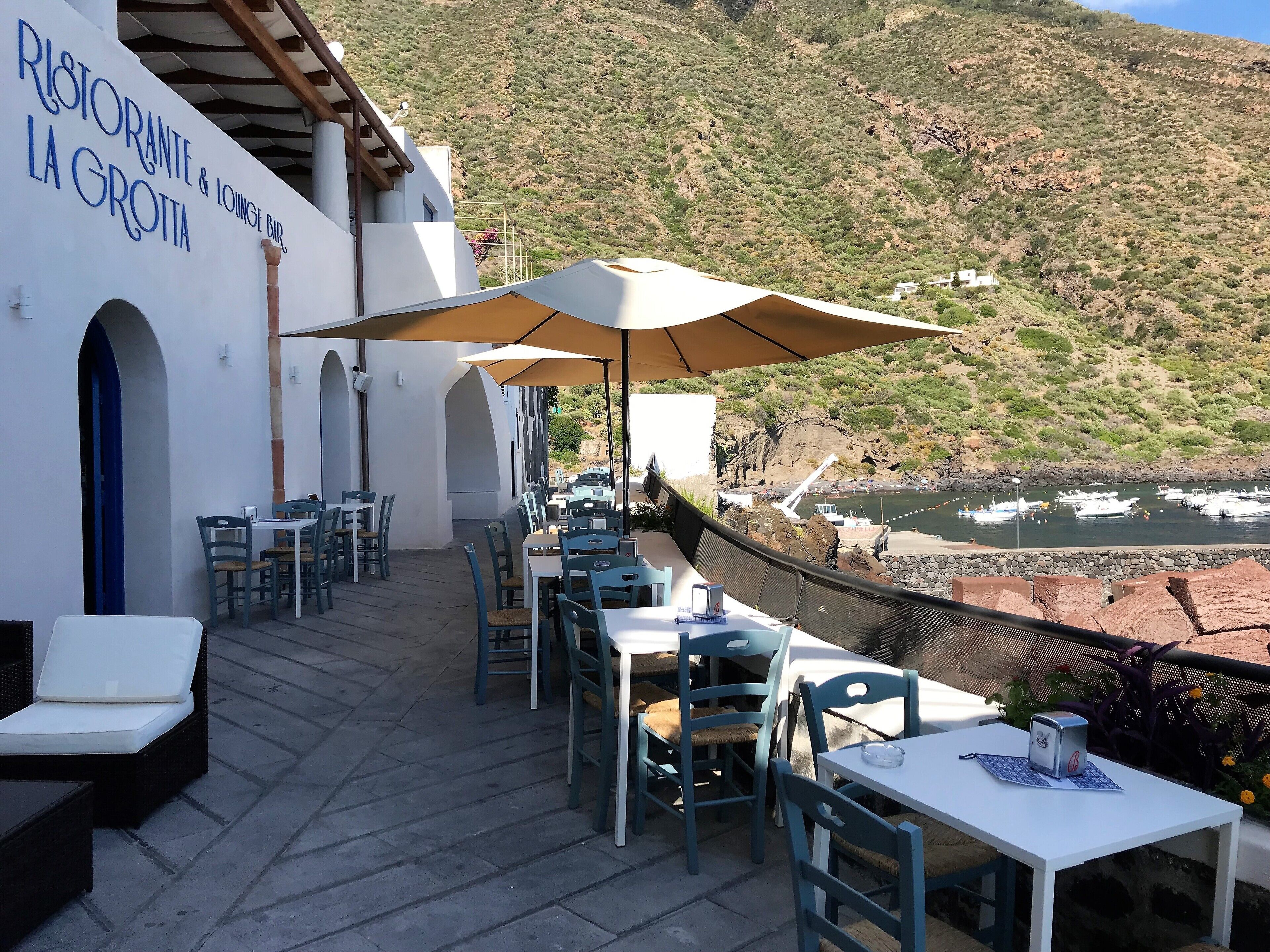 Eine Restaurantterrasse mit Außenbestuhlung, mit Blick auf einen Fluss und Hügel.