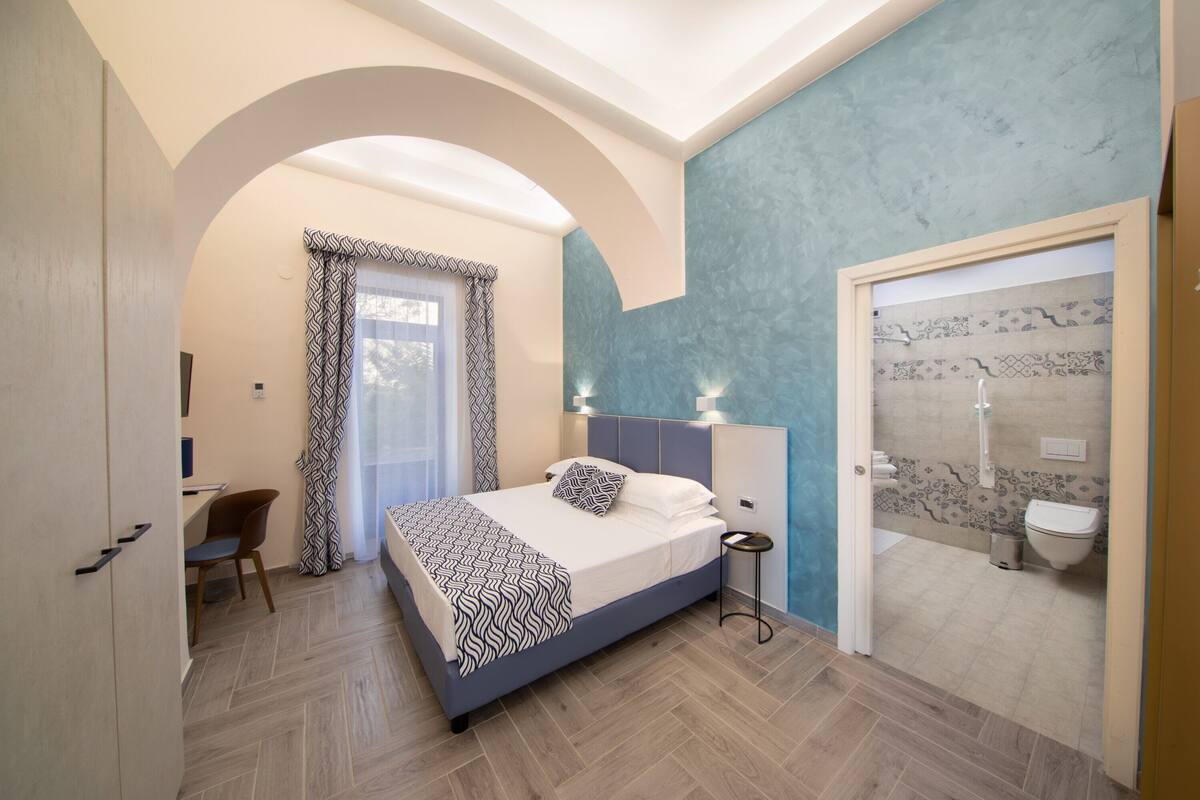 Ein Schlafzimmer mit Bett, Nachttisch und Blick ins Badezimmer.