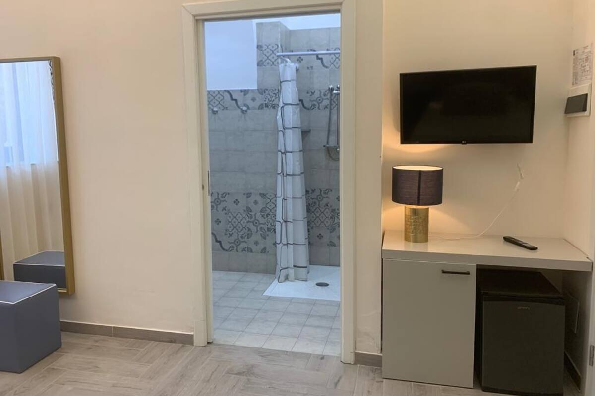 Ein modernes Badezimmer mit Dusche, einem an der Wand montierten Fernseher und einem Schreibtisch mit Lampe.