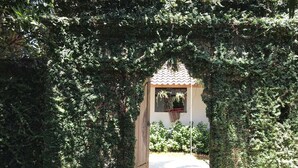 An arched entrance with dense ivy covering, leading to a building with a tiled roof and a window with hanging plants. - Coconut Lodge (Mlonggo)