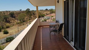 A balcony with a table and chairs, a view of a hilly landscape, and a building with a tiled floor. - Luxury 4 bedroom villa (Monte Francisco)