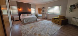 A bedroom with a bed, bedside tables, a large rug, a sofa, and a window with blinds. - Luxury 4 bedroom villa (Monte Francisco)