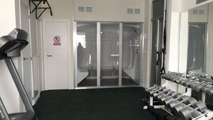 Une salle de sport équipée d’un tapis de course, d’un banc de musculation et d’haltères.