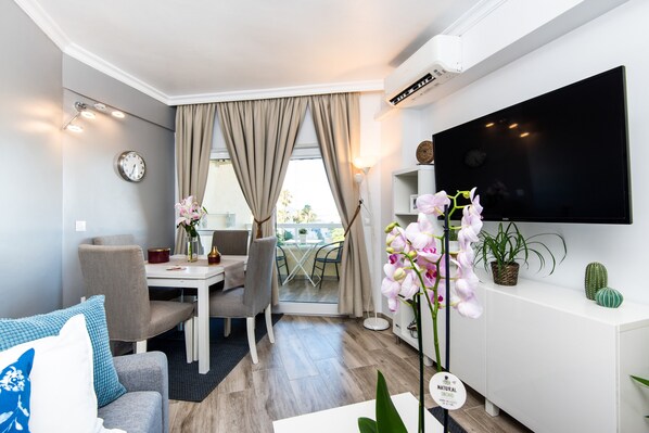 Ein modernes Hotelzimmer mit Flachbildfernseher, Essecke und Balkon mit Vorhängen.
