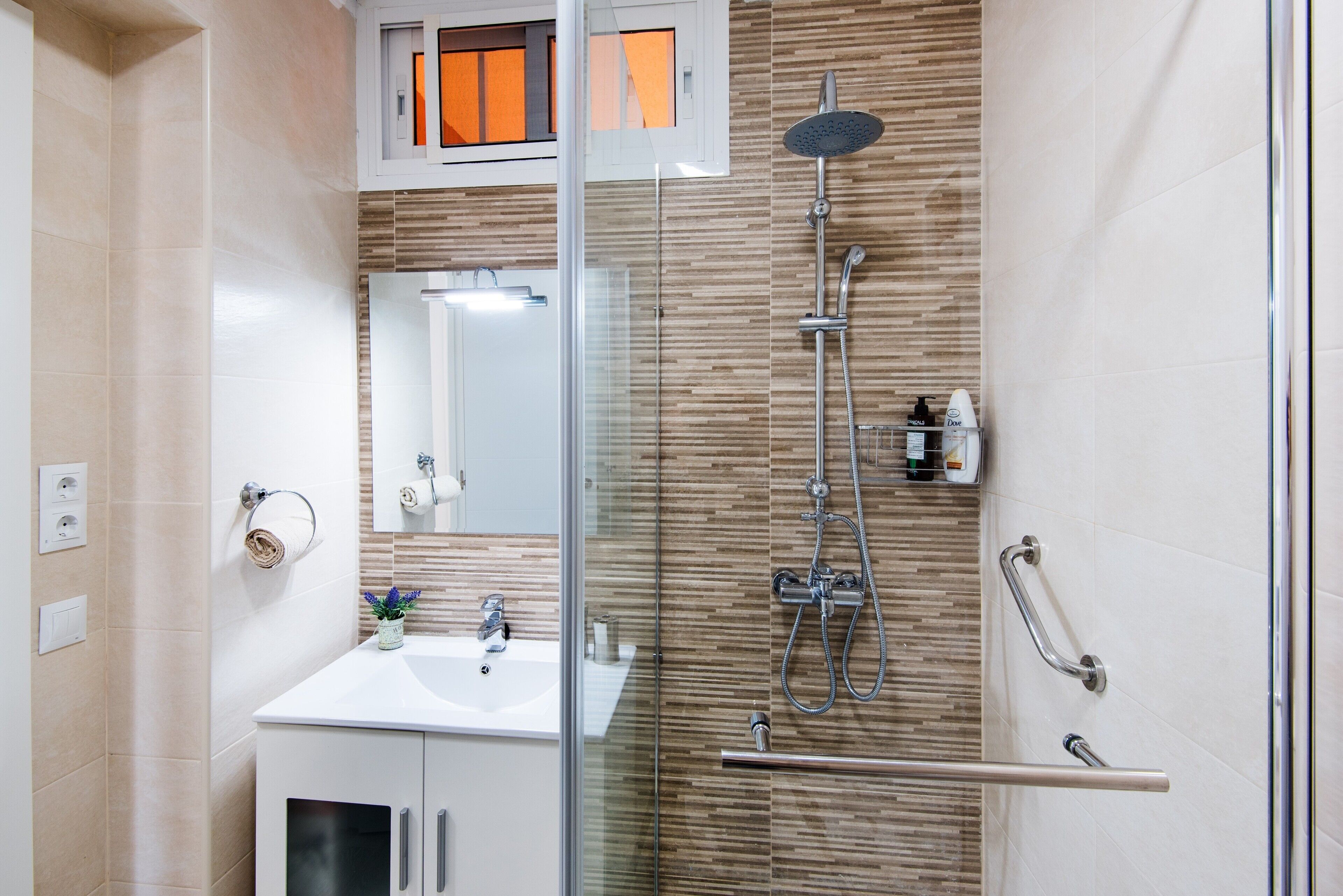 A modern bathroom with a glass shower enclosure, a sink, and a mirror.