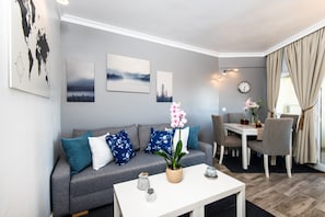 A modern living room with a grey sofa, blue floral cushions, a white coffee table, and a dining area with a table and chairs.