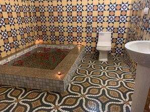 A bathroom with a patterned floor, a bathtub with red flowers, a toilet, and a sink.
