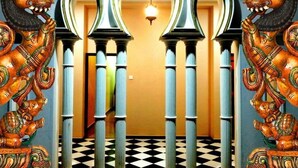 Un pasillo con columnas ornamentadas y detalles decorativos que conduce a una habitación con piso a cuadros y una lámpara colgante.