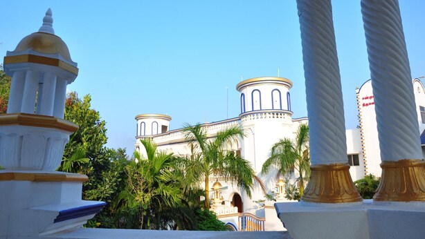 Un edificio con una cúpula y dos torres cilíndricas, rodeado de palmeras y columnas.