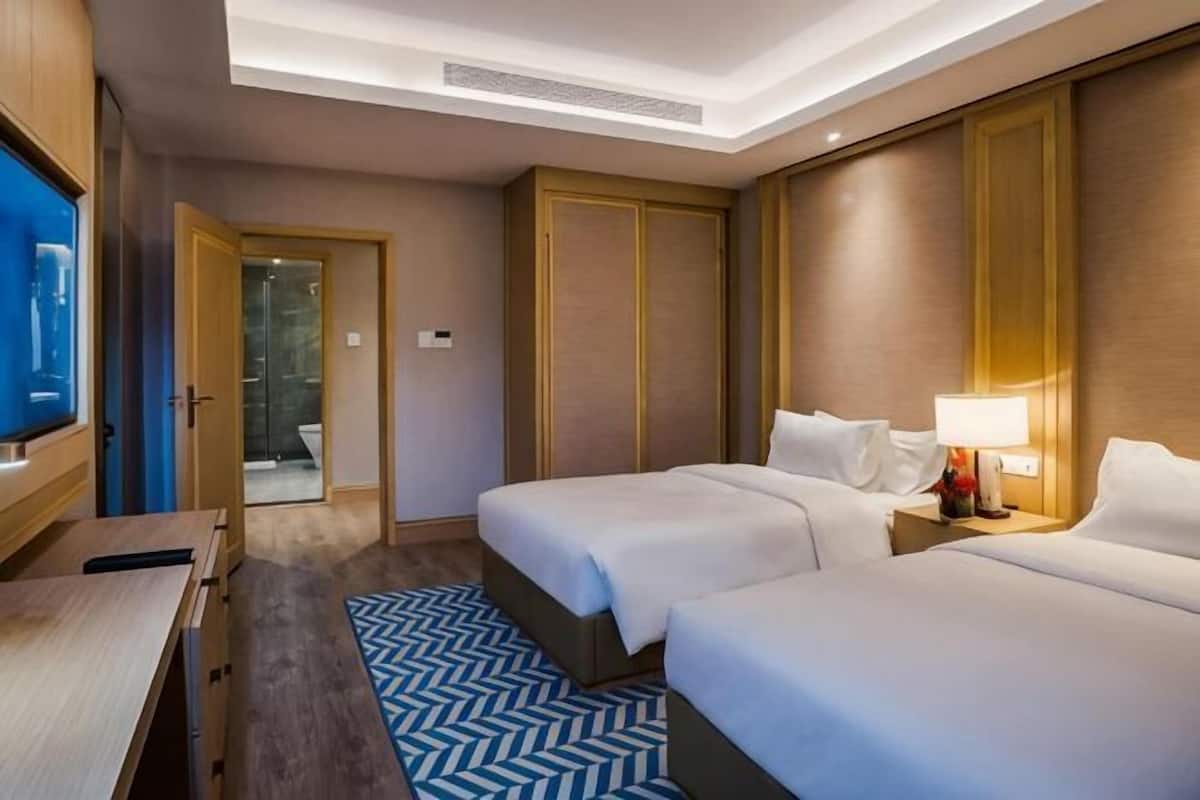 A hotel room with two beds, a desk, a TV, and a bathroom visible through an open door.