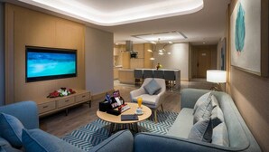Una habitación de hotel moderna con televisión de pantalla plana, sofá, zona de comedor y cocina.