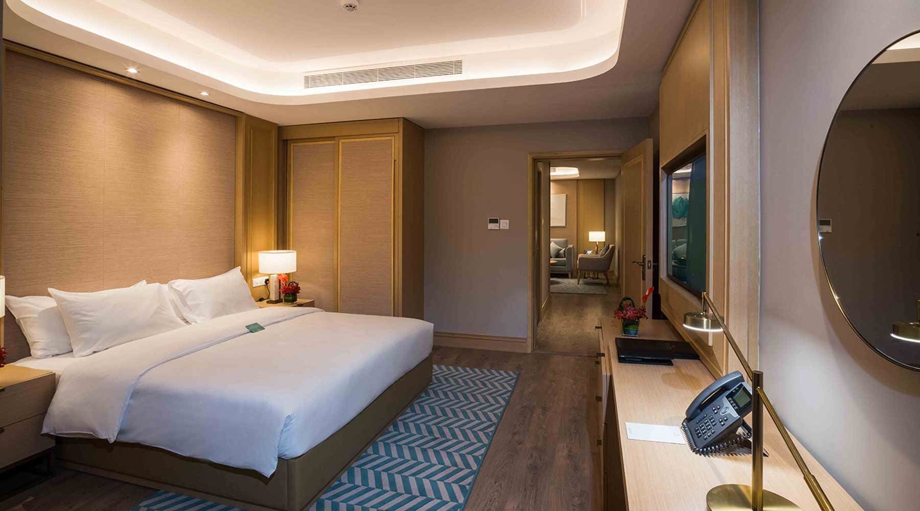 A hotel room with a large bed, a desk with a telephone, a mirror, and a television.