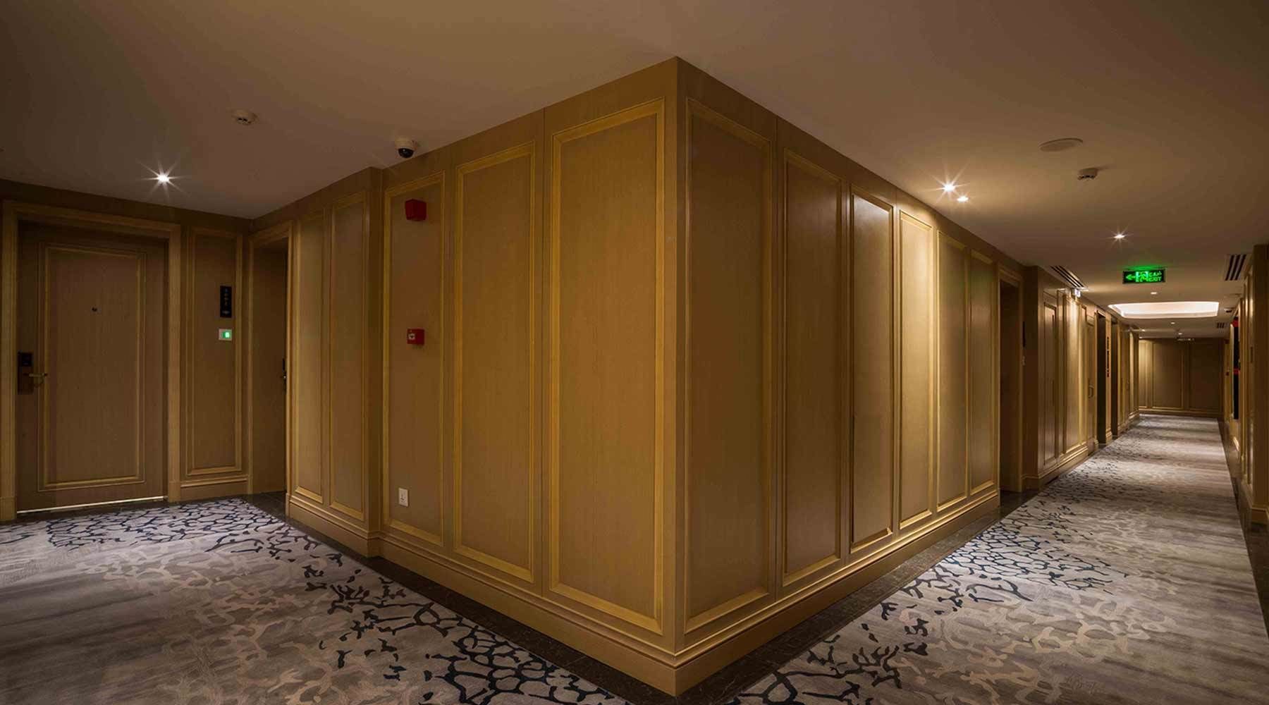 Un corridoio d'albergo con pannelli in legno, pavimento rivestito di moquette e indicazioni di uscita di sicurezza.