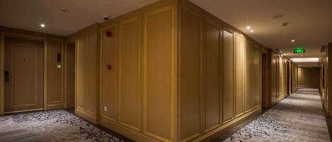 Un corridoio d'albergo con pannelli in legno, pavimento rivestito di moquette e indicazioni di uscita di sicurezza.