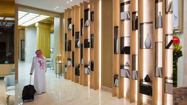 Un moderno vestíbulo de hotel con un pasillo central, una recepción y una pared decorativa con estantes.