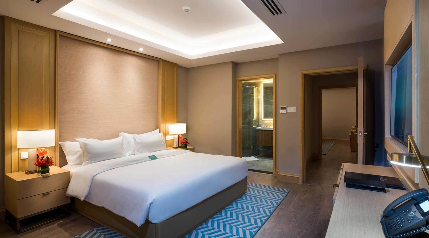 A hotel room with a large bed, bedside lamps, a desk with a phone, and a bathroom visible through an open door.