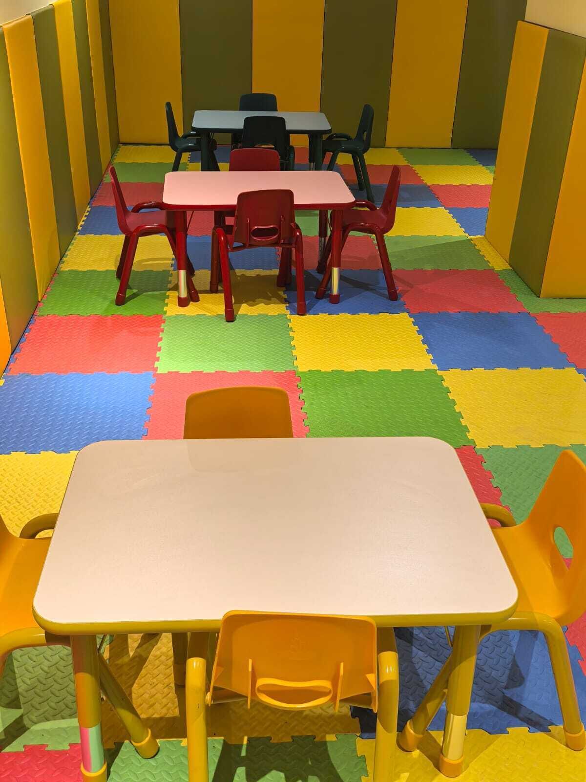 A playroom with colorful foam mats, a white table, and red and yellow chairs.
