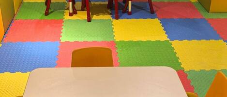 A playroom with colorful foam mats, a white table, and red and yellow chairs.