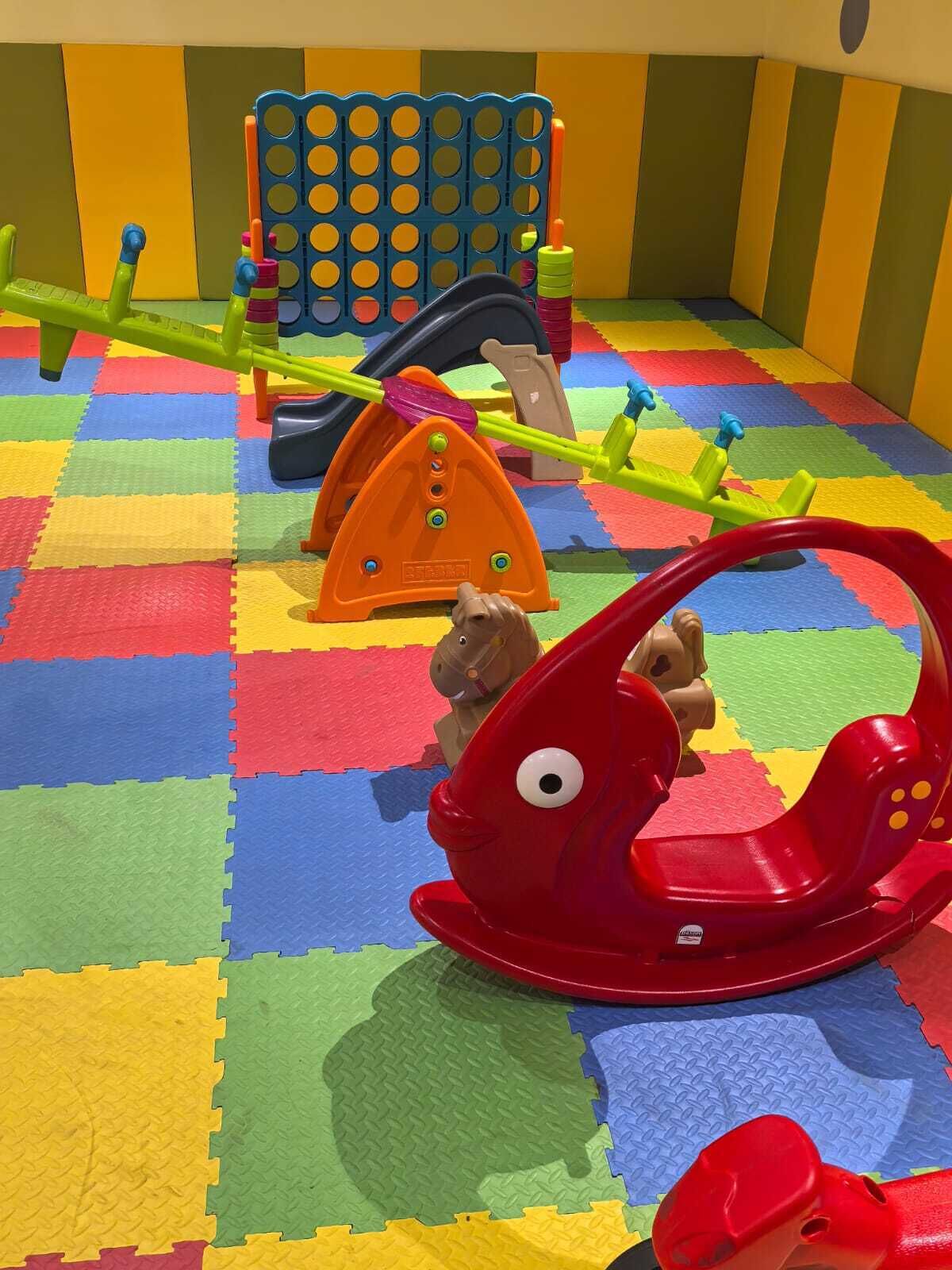 A play area with a colorful checkered floor, a red rocking horse, and various play structures.